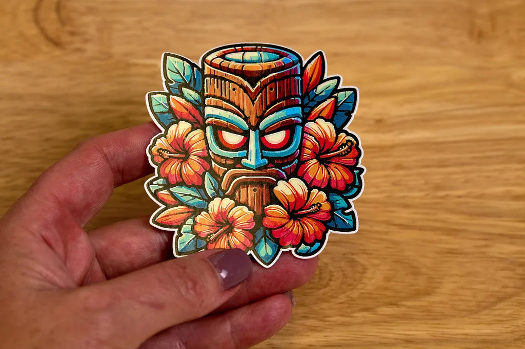 Colorful tiki mask sticker held by a hand on a wooden surface