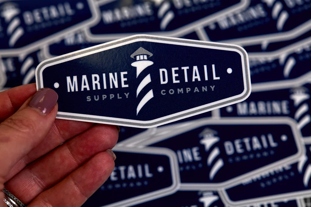 Sticker with 'Marine Detail Supply Company' logo held by a hand against a patterned background.