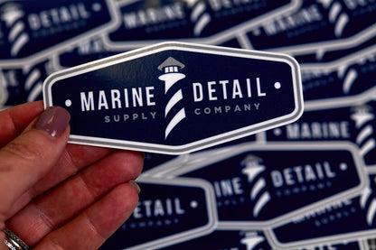 Sticker with 'Marine Detail Supply Company' logo held by a hand against a patterned background.