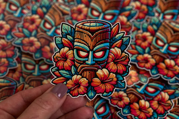 Colorful tiki mask sticker held by a hand against a matching background