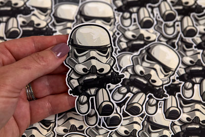 Stormtrooper sticker being held by a hand in front of a pile of stickers.