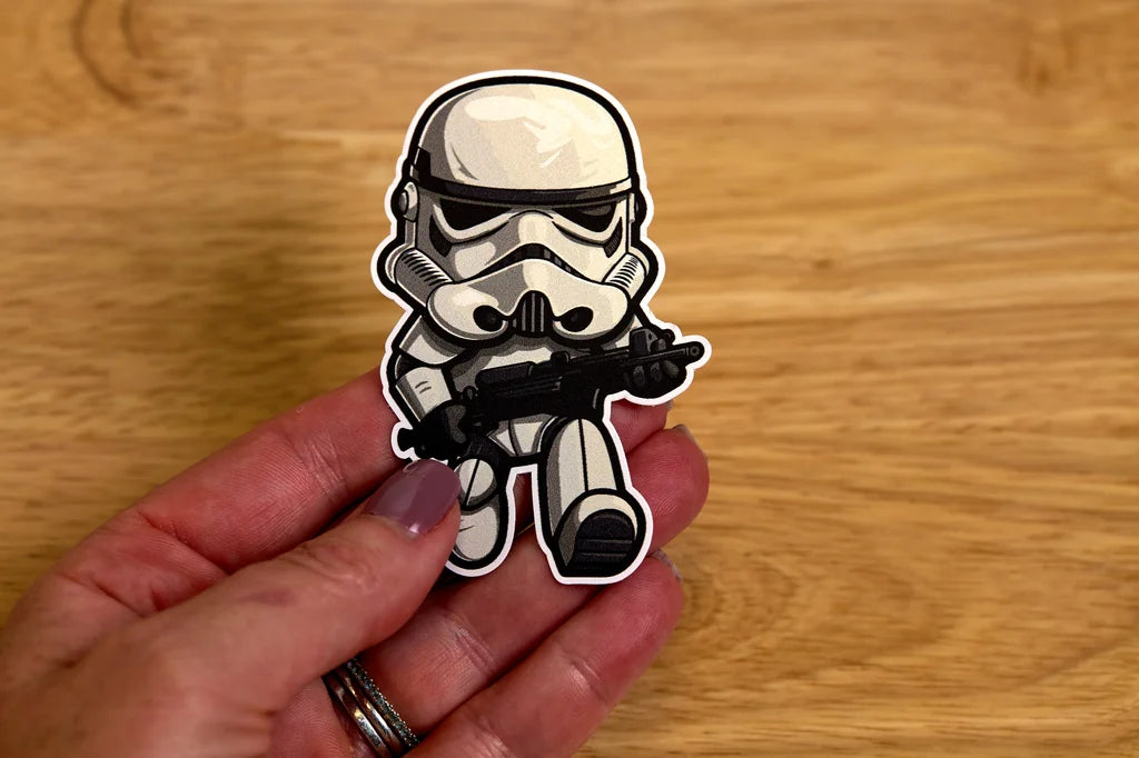 Sticker of a stormtrooper character held by a hand on a wooden surface