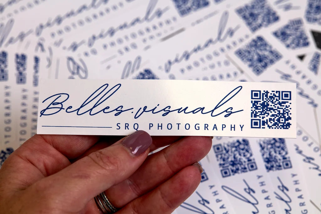 Hand holding a business card sticker with 'Belles Visuals SRQ Photography' branding.