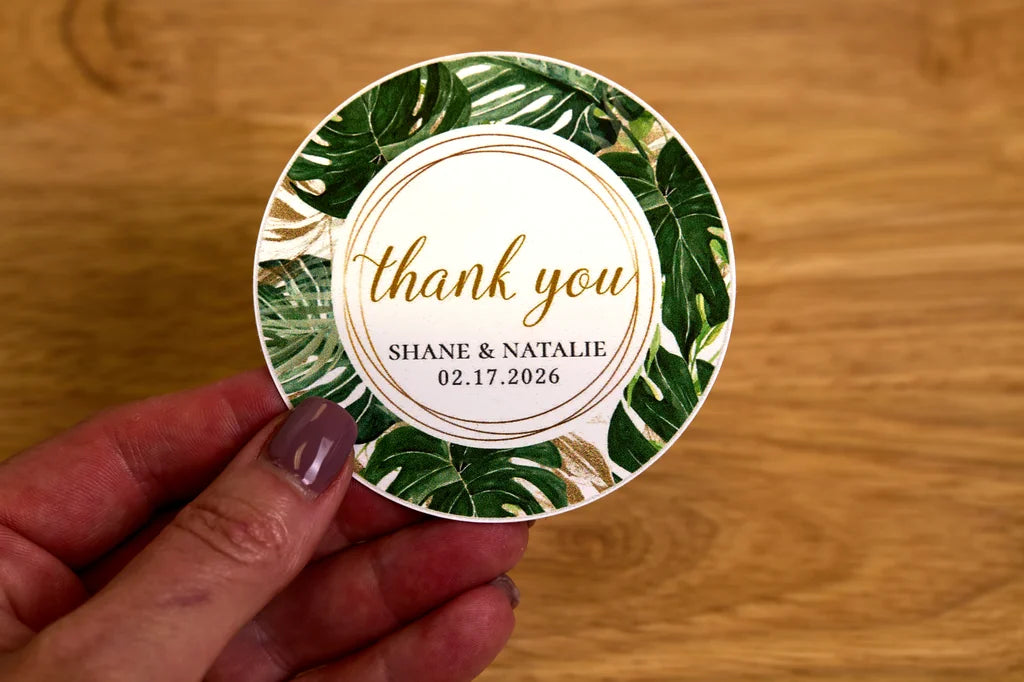 Round sticker with 'thank you' text held by a hand on a wooden surface