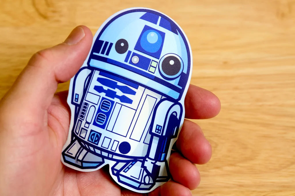 Hand holding a blue and white R2-D2 sticker on a wooden surface