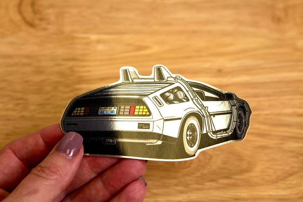 Mirror chrome sticker of delorean held by a hand on a wooden surface