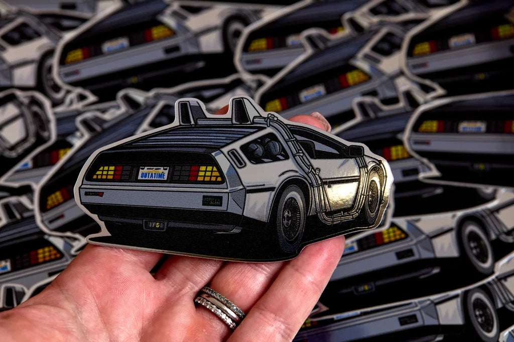 Silver delorean chrome sticker held above a pile of stickers.