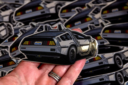 Silver delorean chrome sticker held above a pile of stickers.